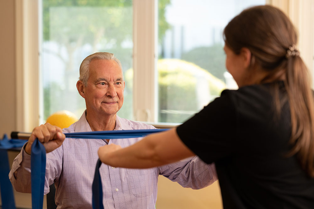 Male resident using resistance bands with physical therapist